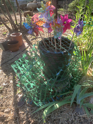 A handmade lizard habitat barrier with bright pinwheels, green mesh, and stones — a joyful protection created after my poodle’s first lizard kill